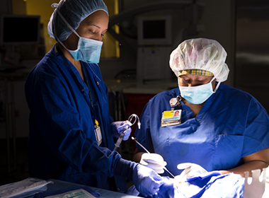Two anesthesia technologists working in an operating room wearing blue scrubs, surgical caps and masks